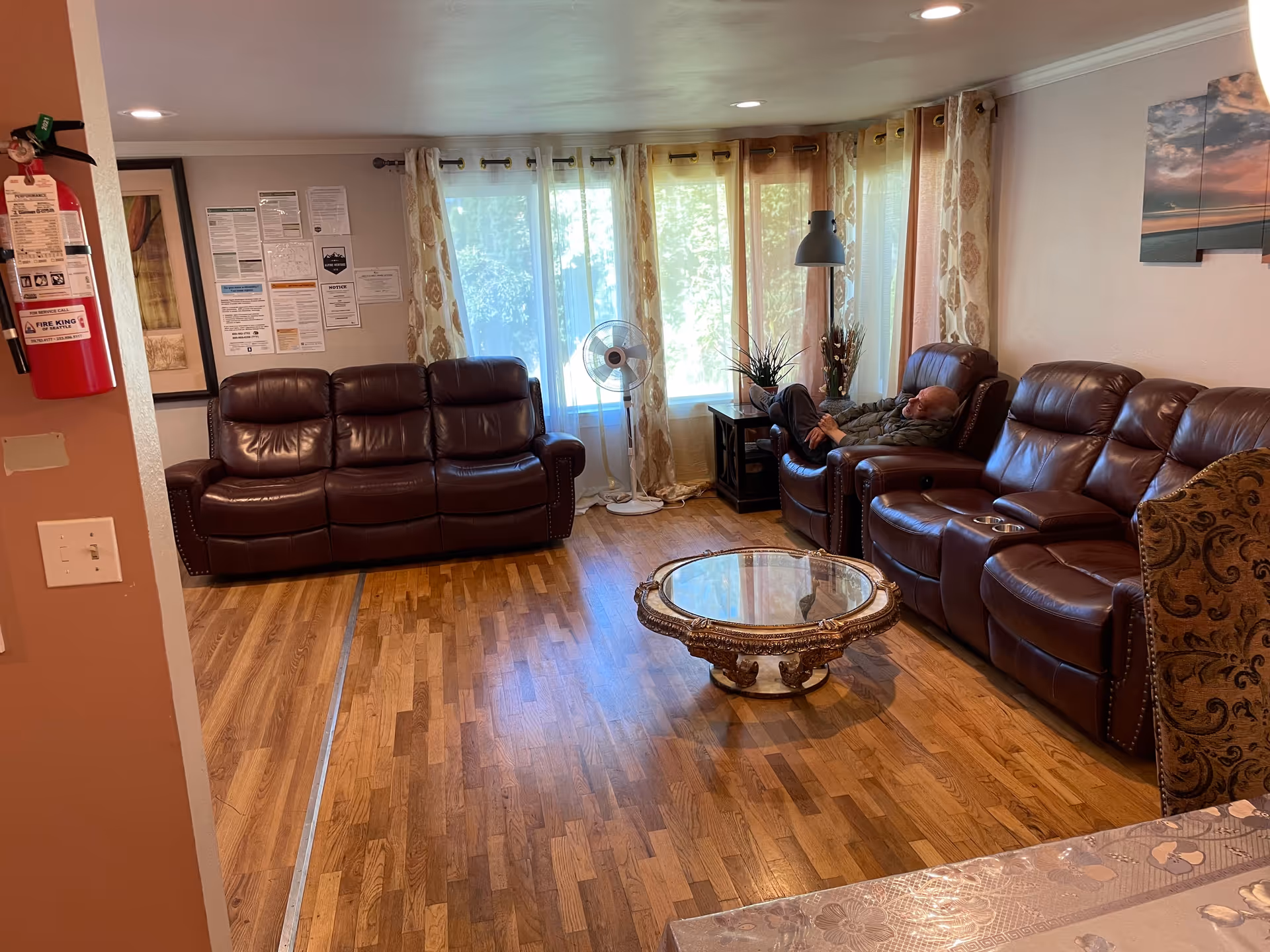 Cozy senior living lounge with leather sofas, a glass coffee table, and a resident resting.