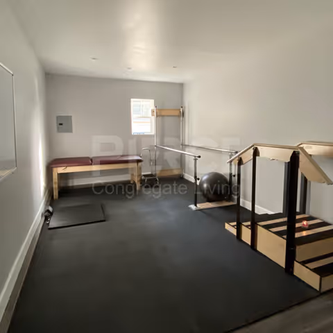 Small indoor exercise room in a senior living facility with bench, stairs, mats, and a window.