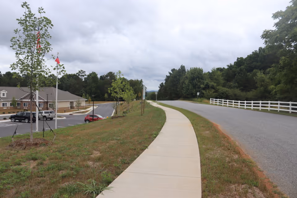 Curved sidewalk along a grassy median leads to Grace Village exterior building and road.