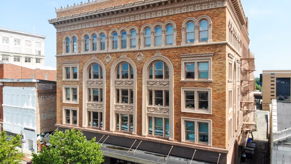 Tall brick building with arched windows and a fire escape on a city street