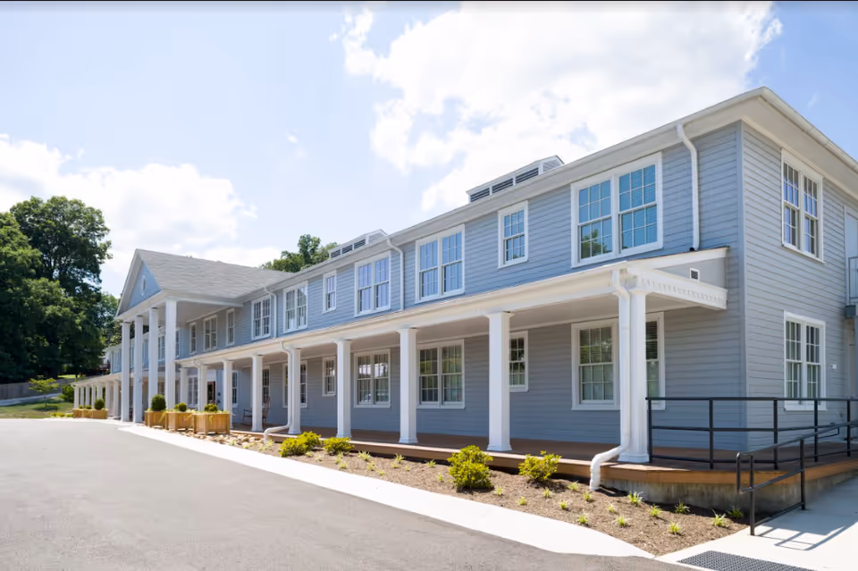Blue two-story senior living building with white columns and a spacious front porch.