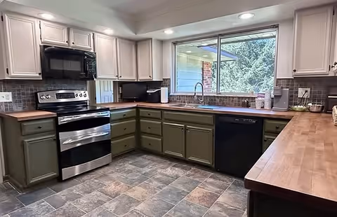 U-shaped kitchen with green lower cabinets, white uppers, stainless appliances, and a window.