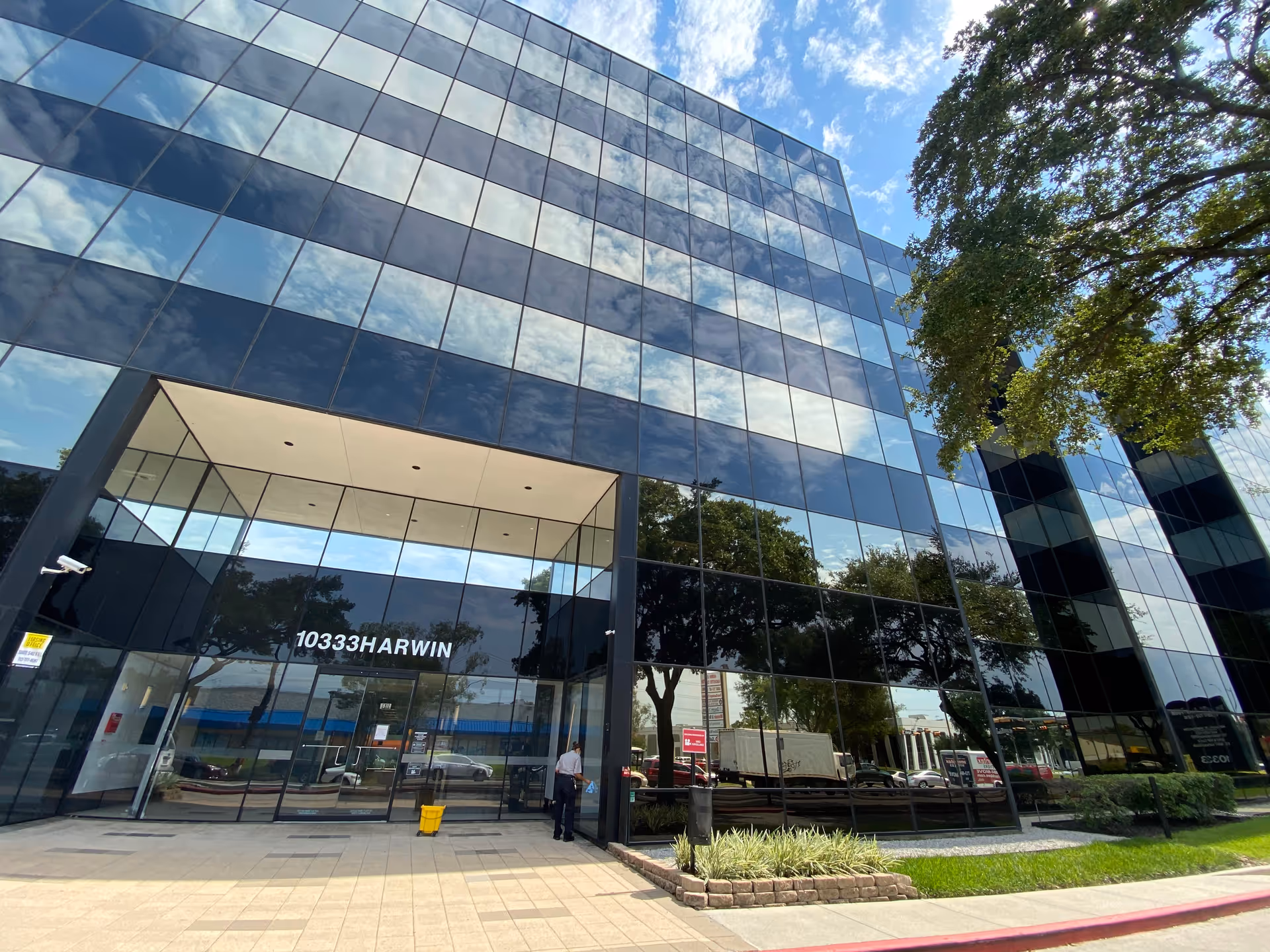 Glass-front modern office building with reflective windows and surrounding trees