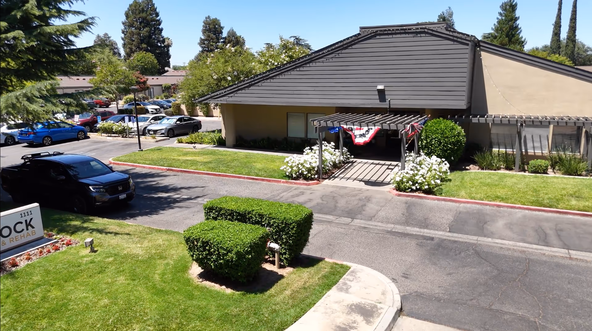 Exterior view of a single-story nursing center with a driveway, cars, and landscaped entrance.