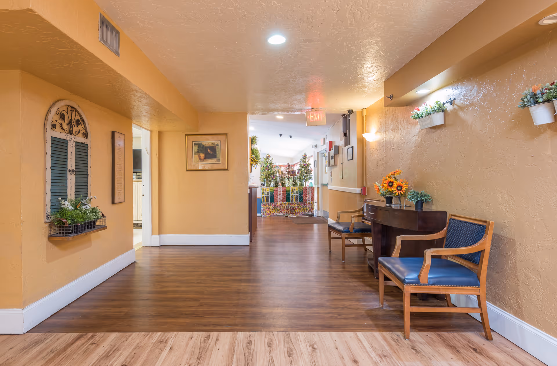 Interior hallway of a senior living facility with seating, plants, and warm walls.