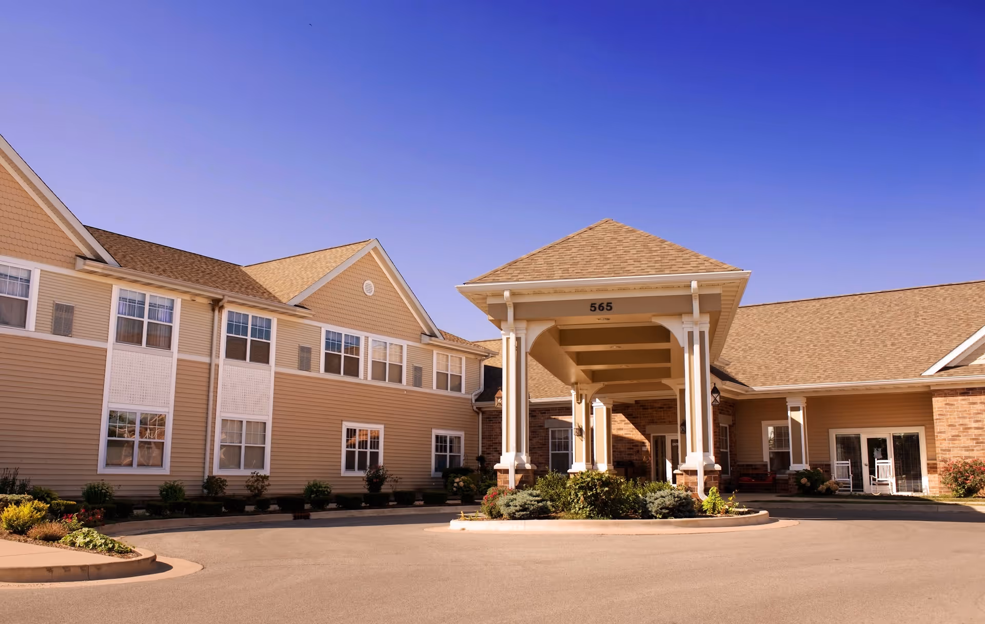Front entrance of a beige senior living facility with a covered porte-cochere and landscaped driveway.