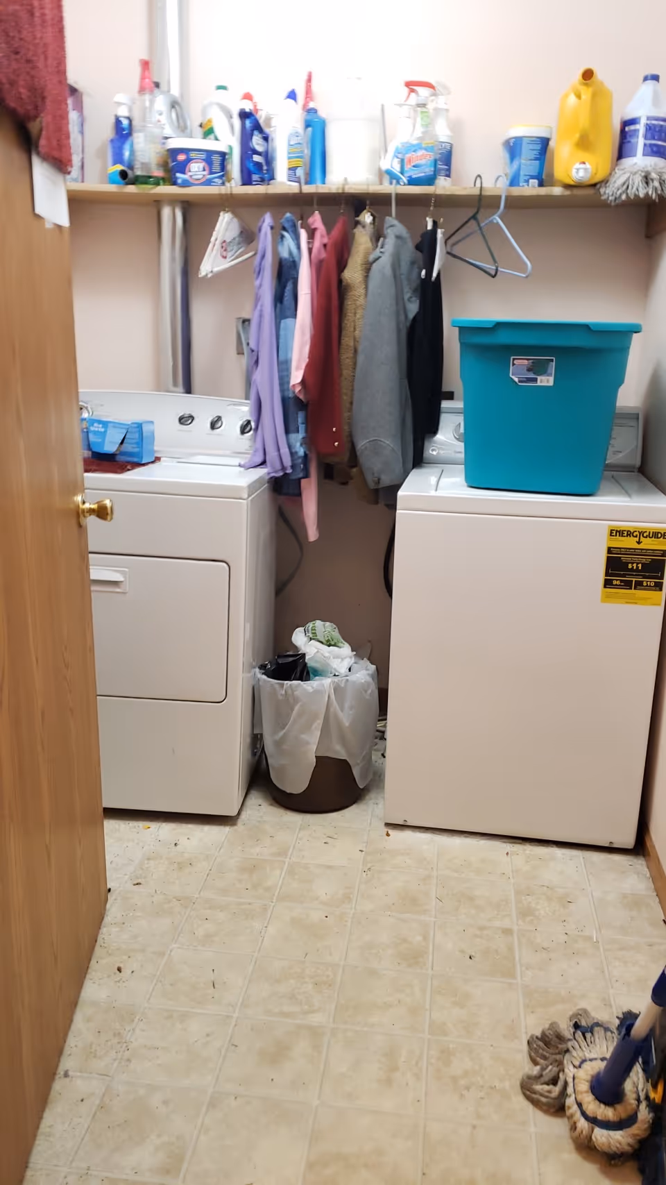 Laundry room with washer, dryer, shelves, clothing, and cleaning supplies.