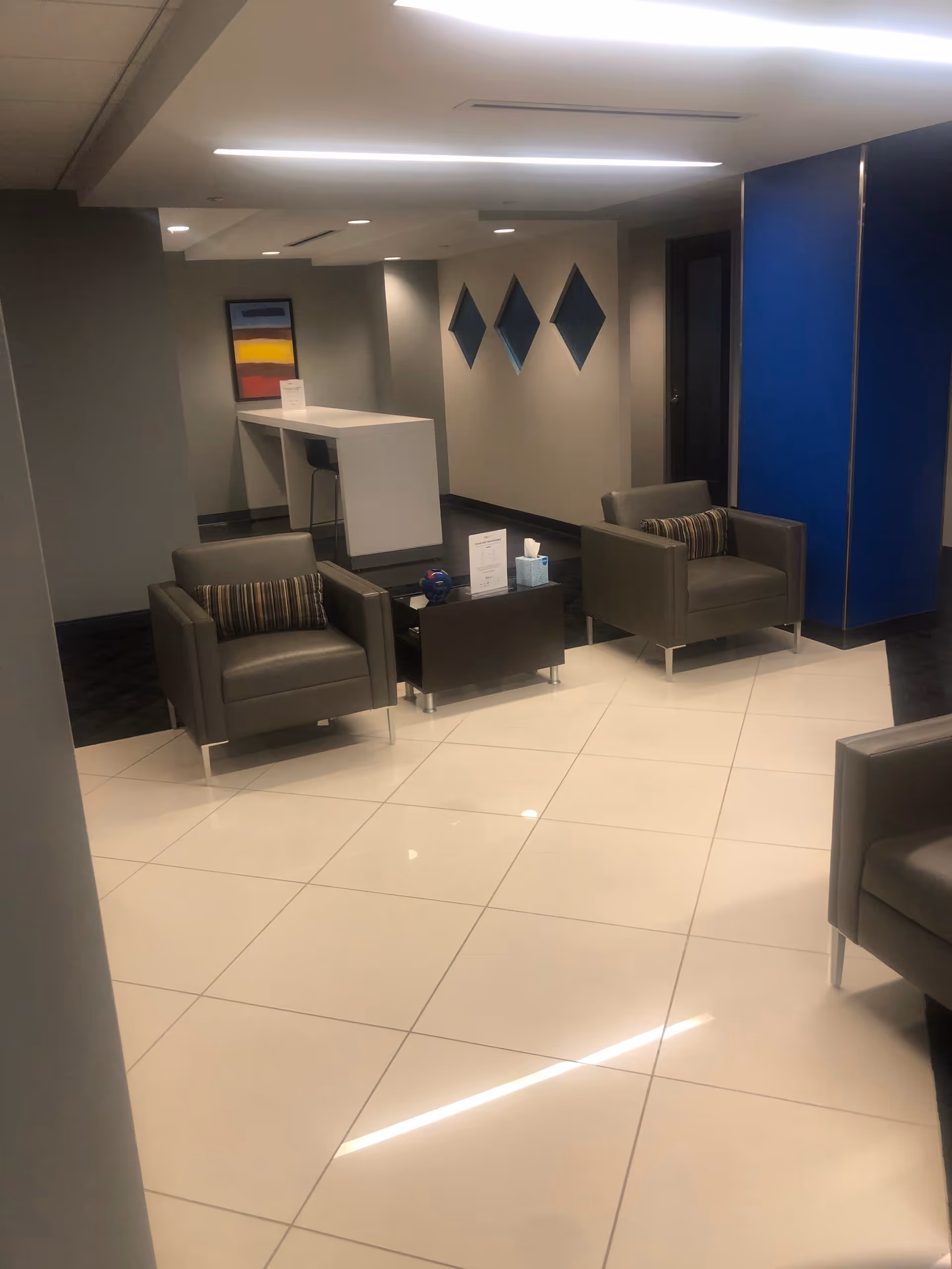 Modern lobby area with gray chairs, white tiled floor, and blue wall panels.