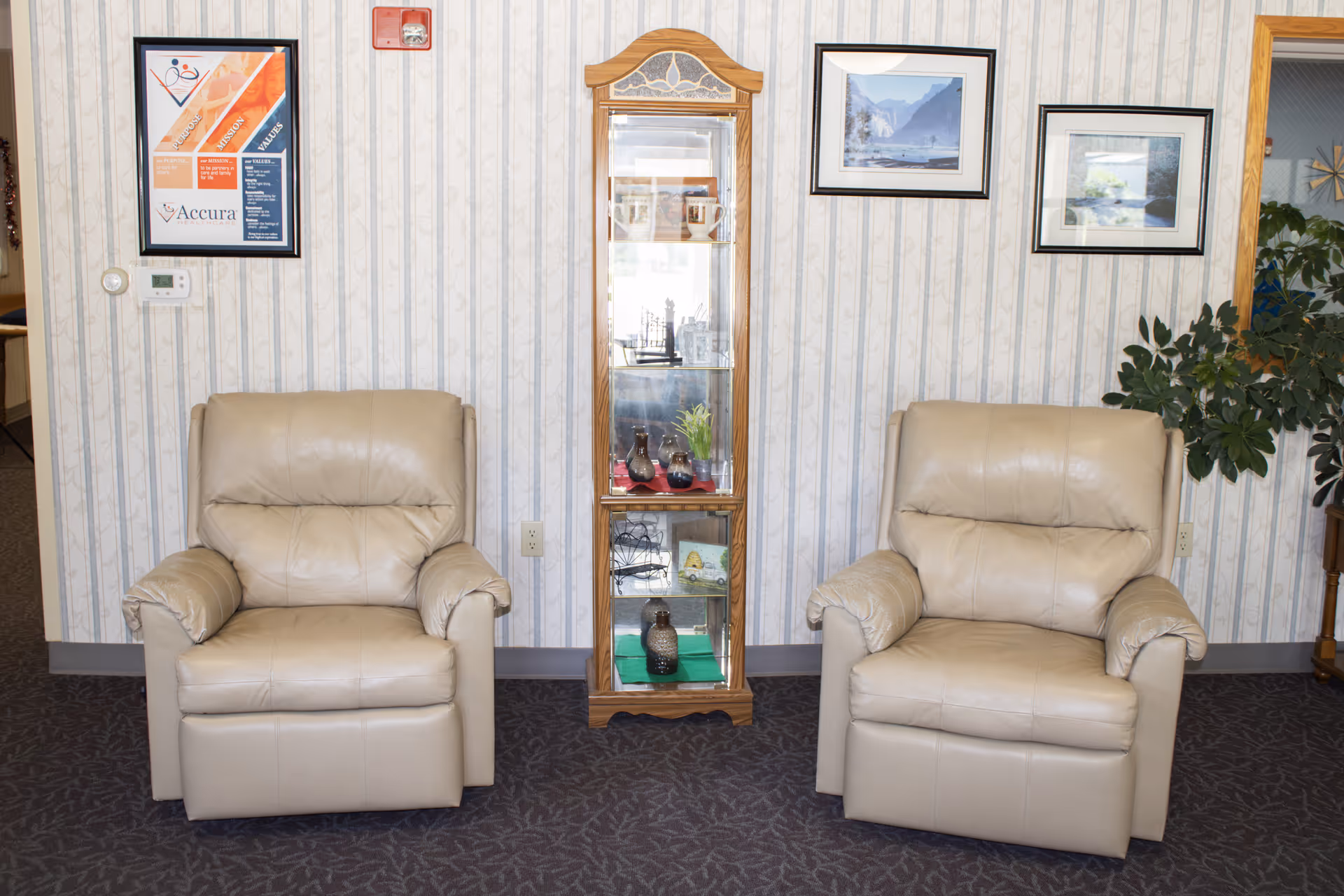 Two beige recliner chairs flank a glass display cabinet in a patterned room.