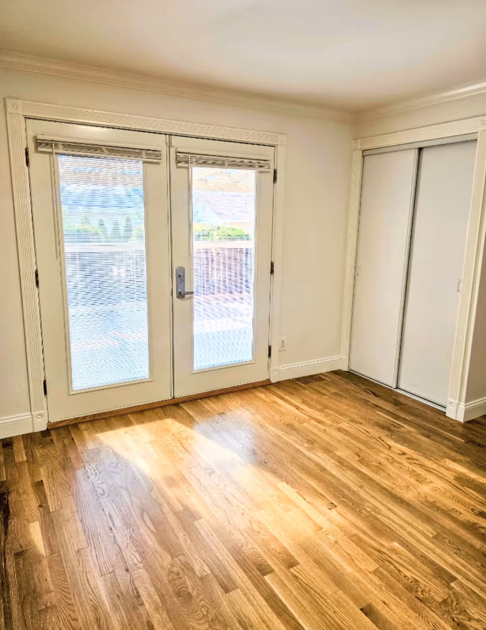 Bright interior room with glass double doors, white walls, and a built-in sliding closet.