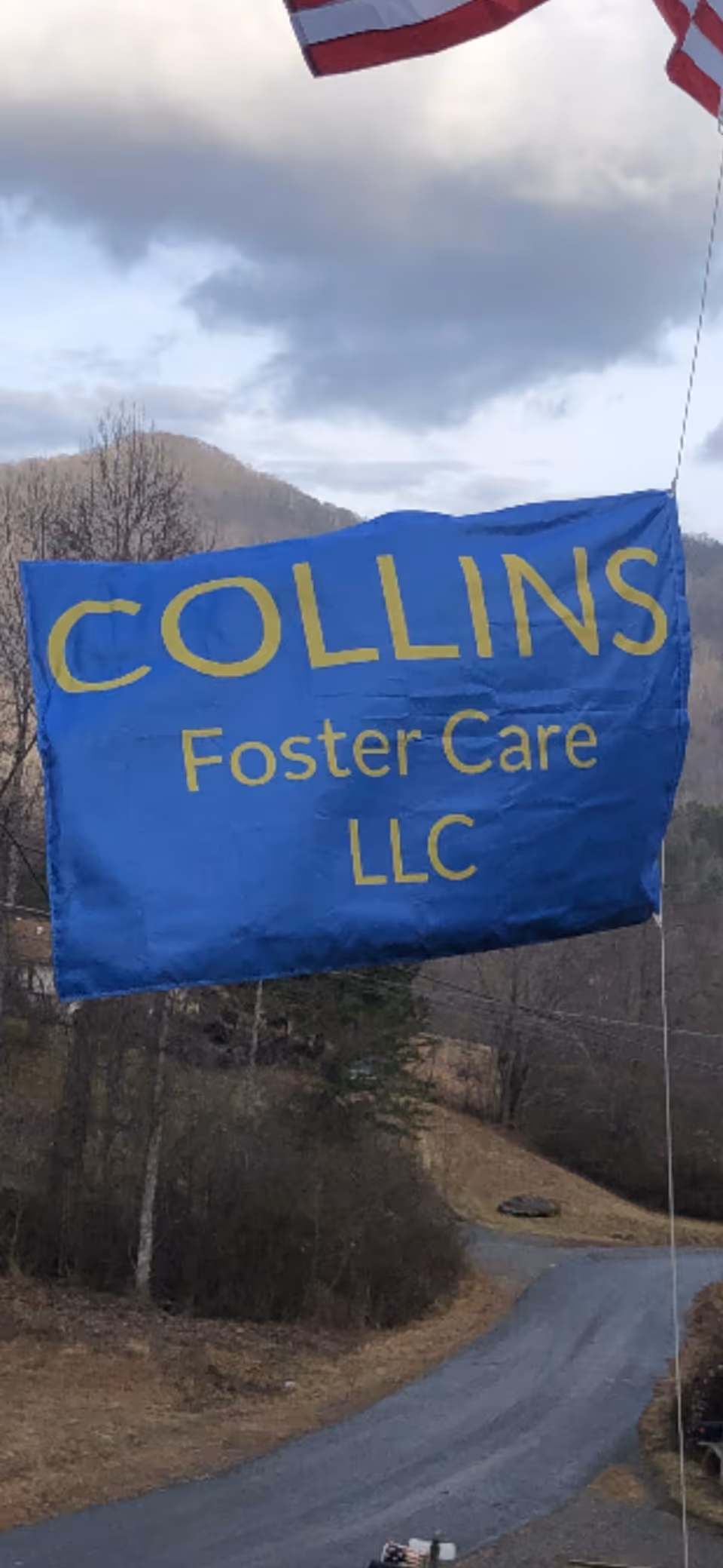 Blue banner reading COLLINS Foster Care LLC hangs outdoors along a winding road.