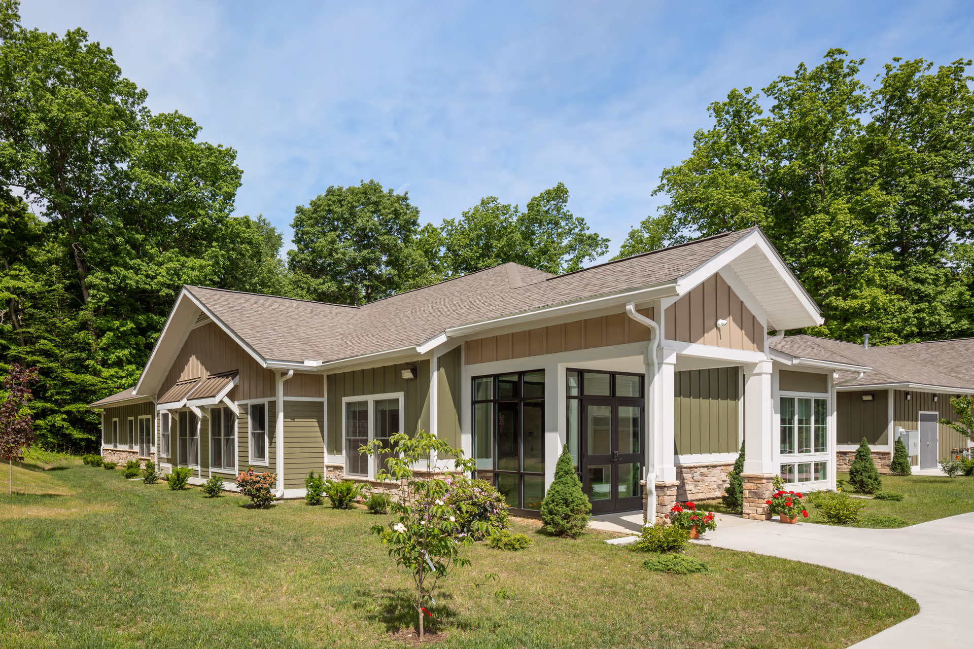 Single-story senior living facility with green siding, stone accents, and a curved entrance walkway.