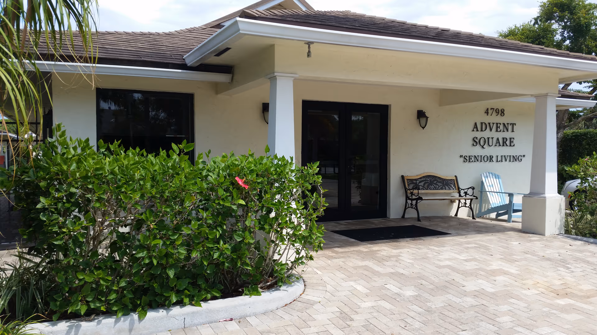 Exterior entrance of Advent Square Senior Living with bench, chairs, and hedges.