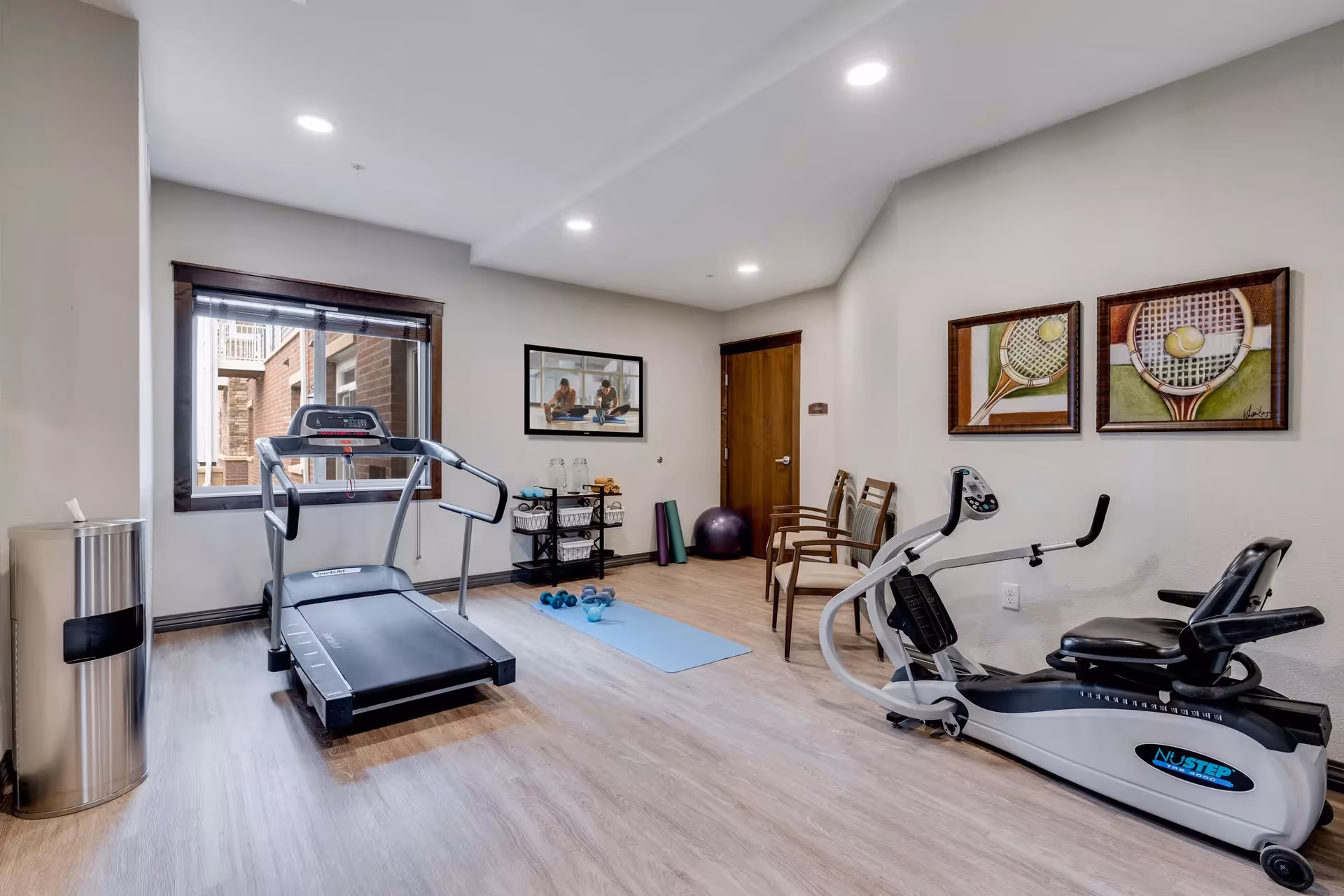 Indoor fitness room with treadmill, stationary bike, mats, and dumbbells.