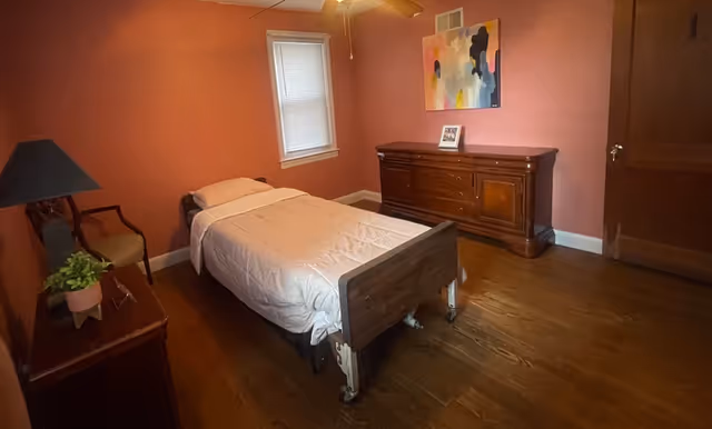 A small bedroom in Heavenly Grace Assisted Living with a single bed, dresser, and pink walls.