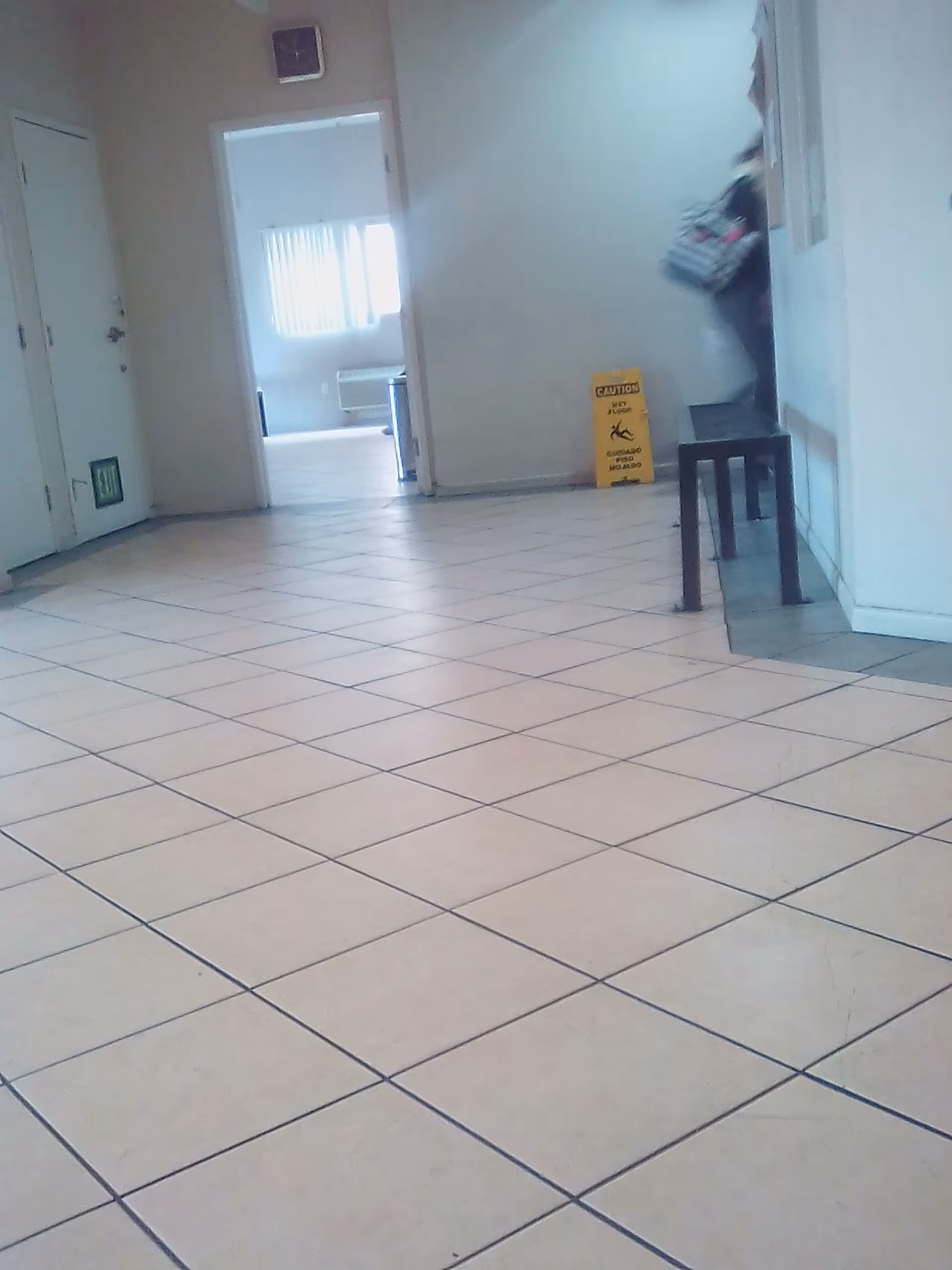 Long tiled indoor hallway in a senior living facility with a wet floor sign and person.