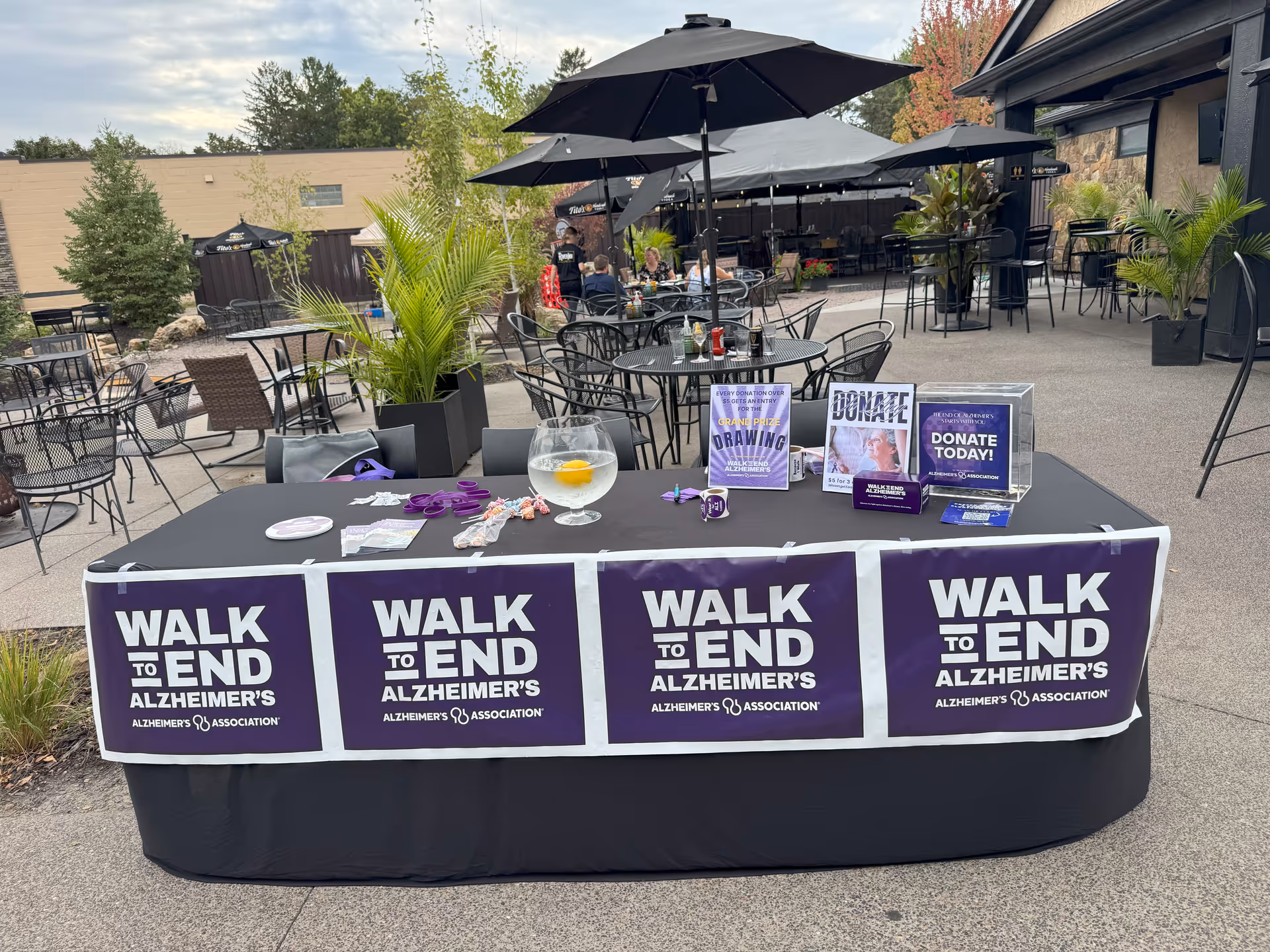 Outdoor patio with tables, umbrellas, and a fundraising table for Walk to End Alzheimer's.