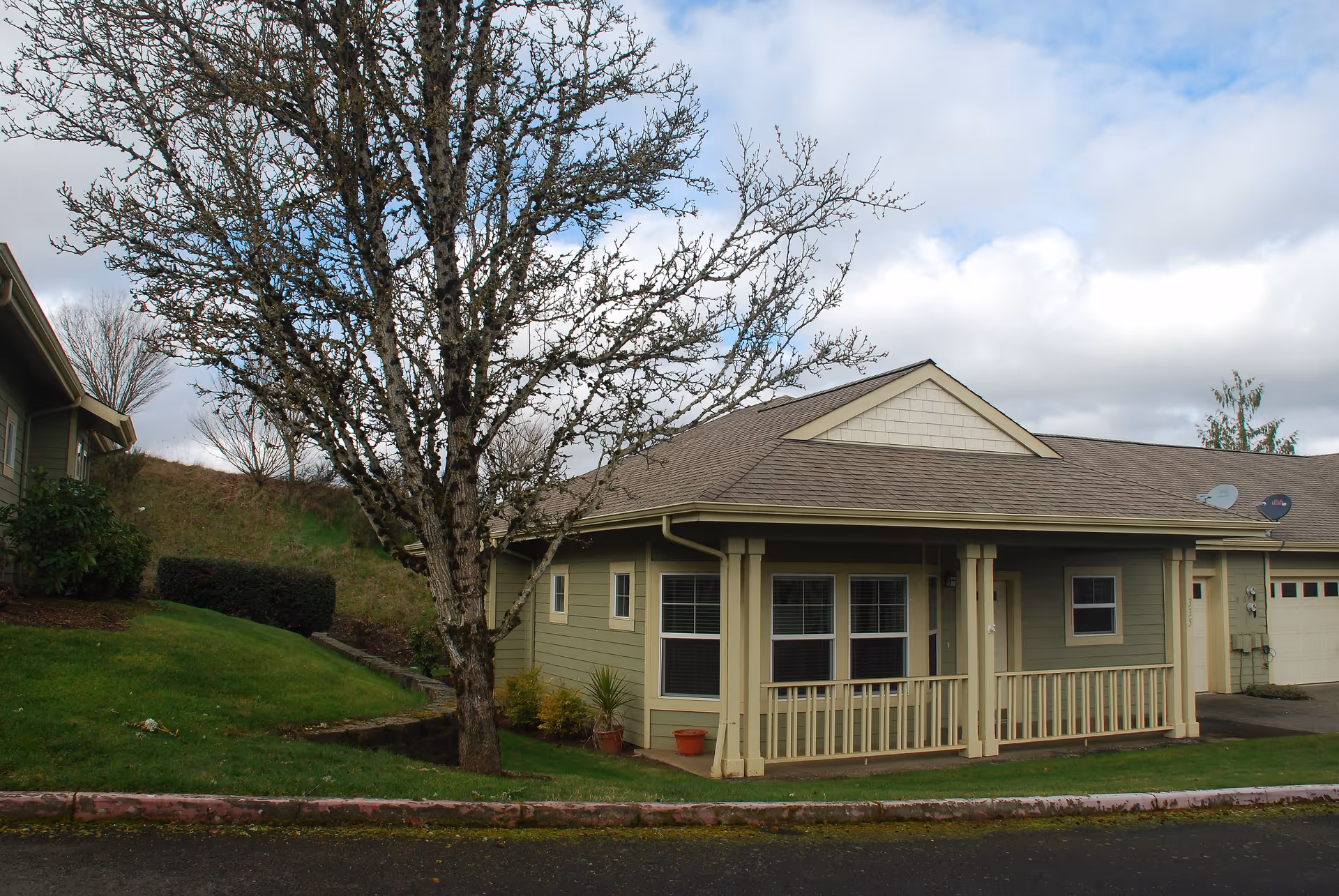 Front exterior of a single-story green building with a covered porch, a leafless tree, and a small lawn.