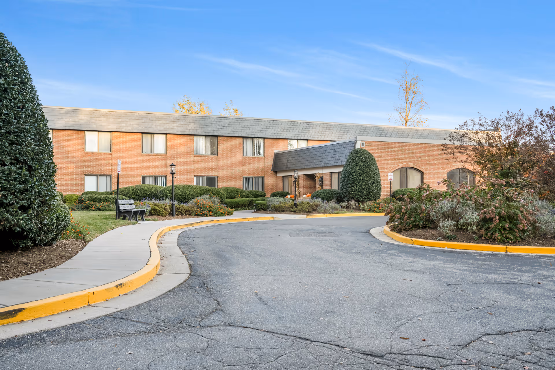 Exterior view of a brick senior living facility with a curved driveway and landscaped grounds.