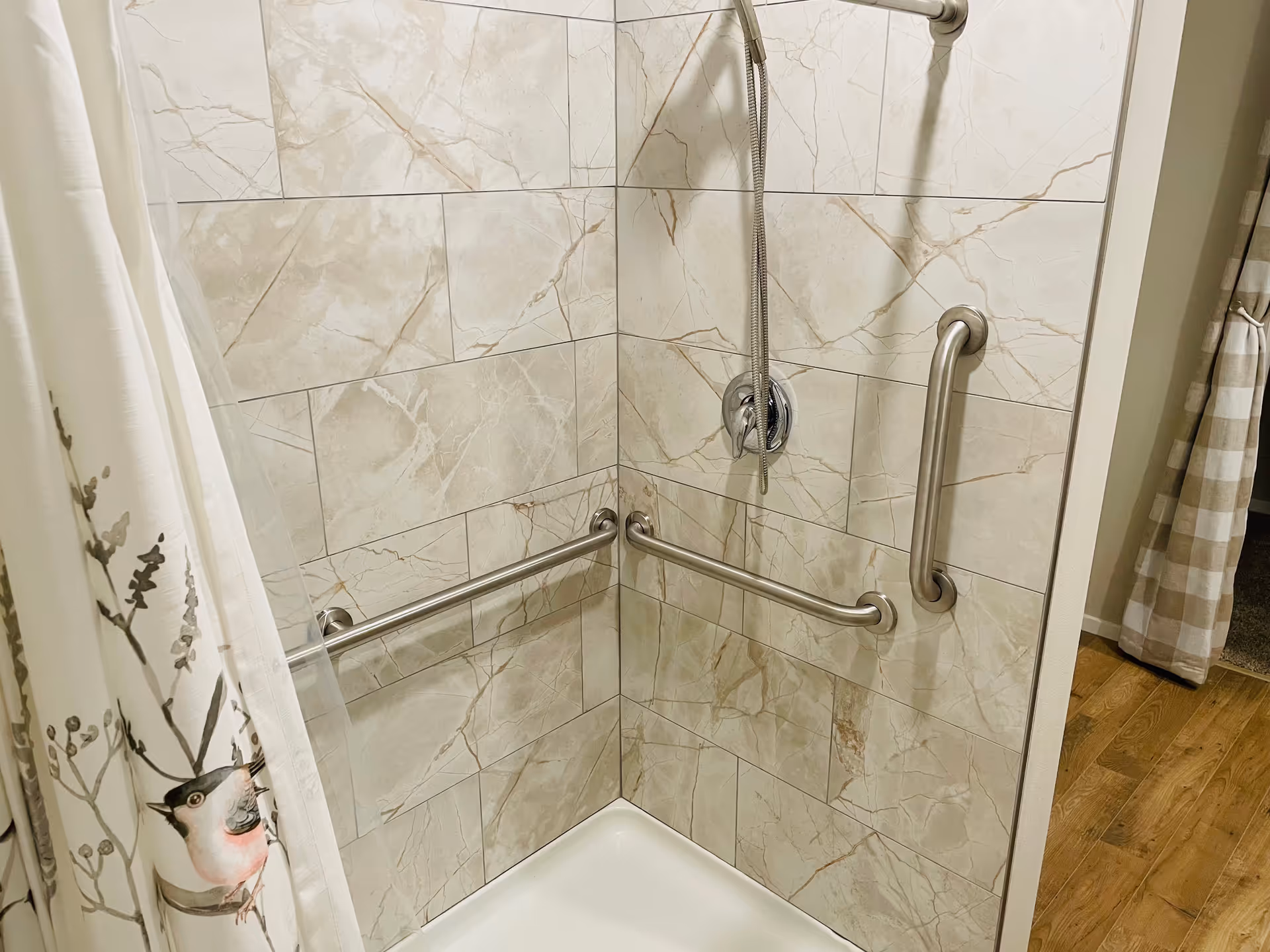 Accessible tiled shower with grab bars, handheld shower, and a decorative curtain.