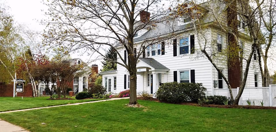 Exterior of a white, two-story house-like senior living building with a manicured front yard.