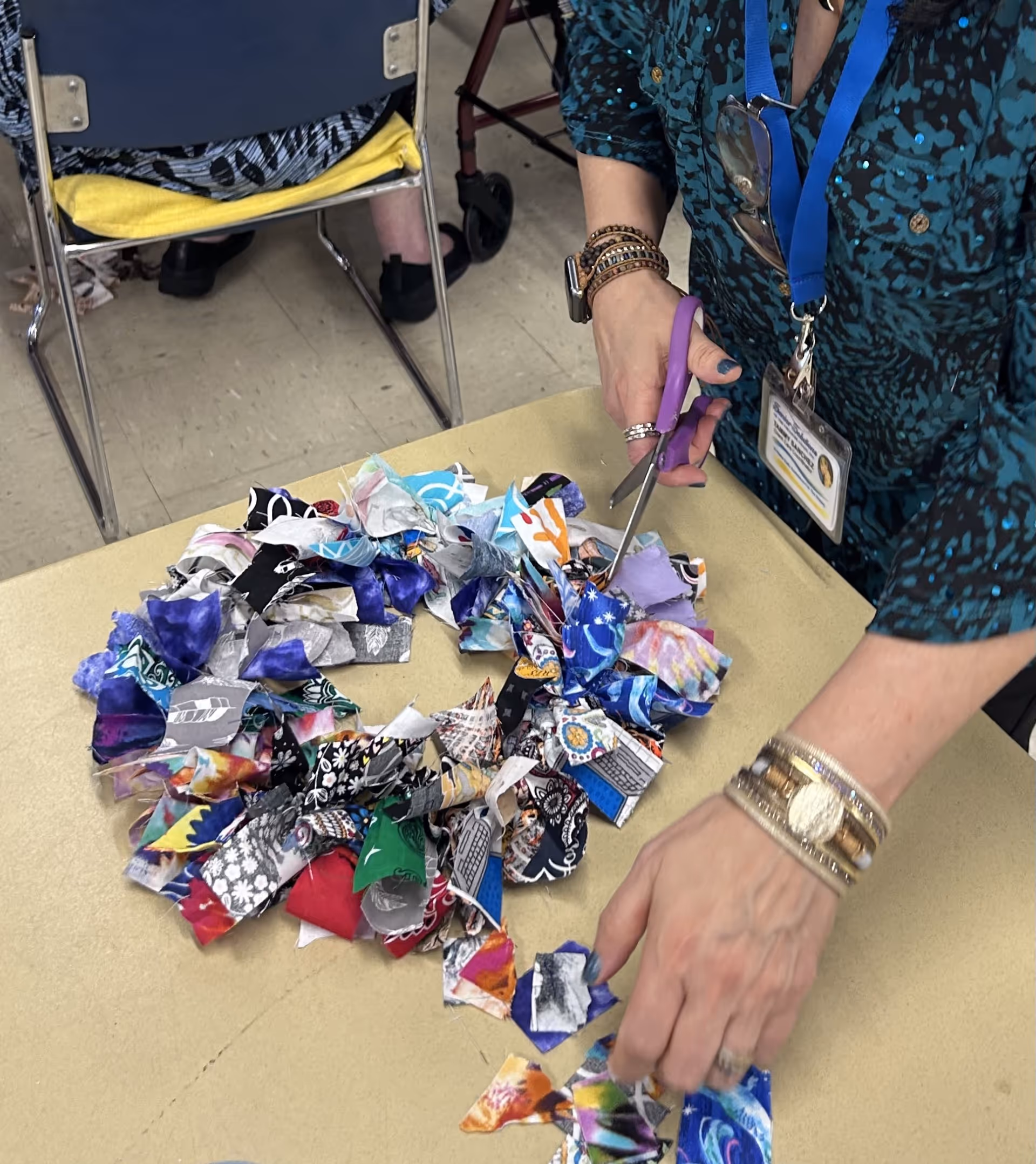 Staff member's hands cut colorful fabric triangles on a table during an indoor craft activity.