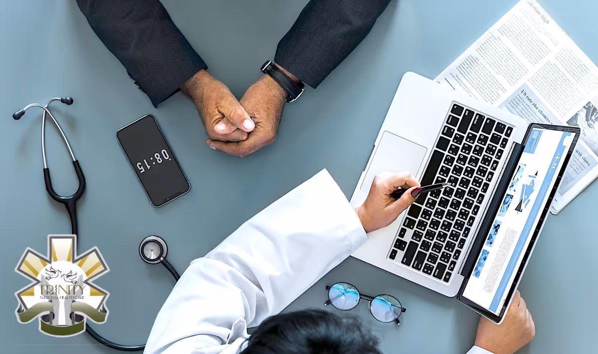 Top-down view of a clinician's hands at a desk with laptop, stethoscope, and papers.
