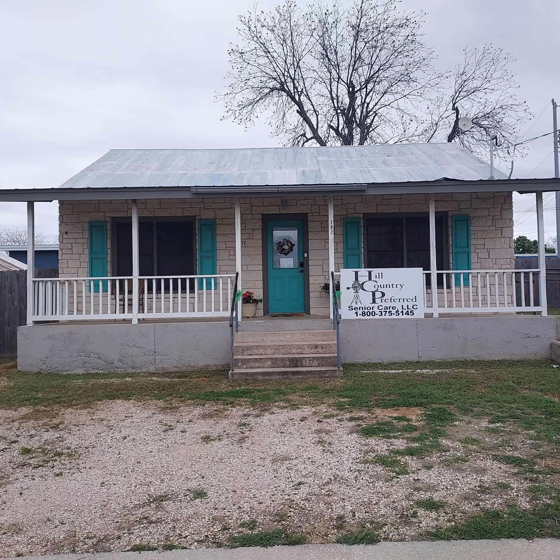 Small stone-front building with teal doors, a wraparound porch, and a sign.