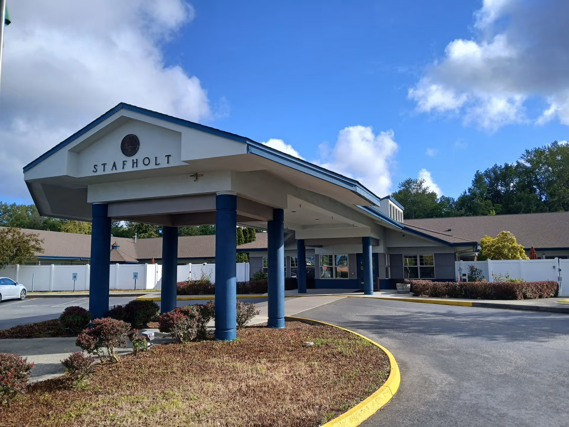 Front entrance of Stafholt Health and Rehabilitation showing a covered drop-off with blue columns and the facility name on the facade.