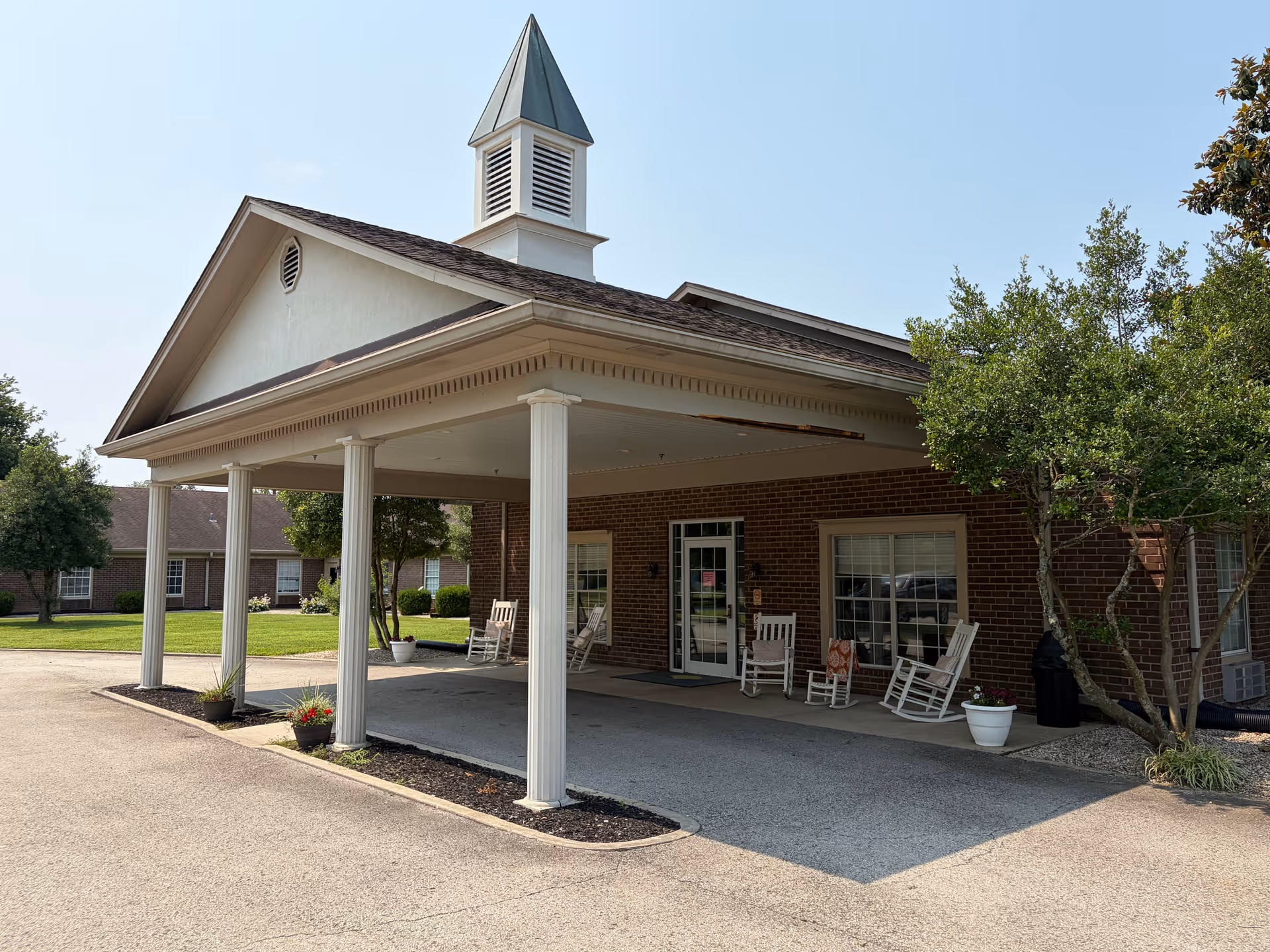 Brick facility entrance with a covered portico and white rocking chairs outside.