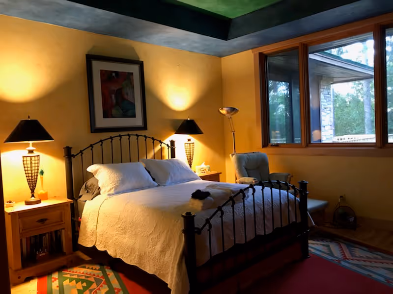Cozy bedroom with iron bed, two nightstands, lamps, and a large window.