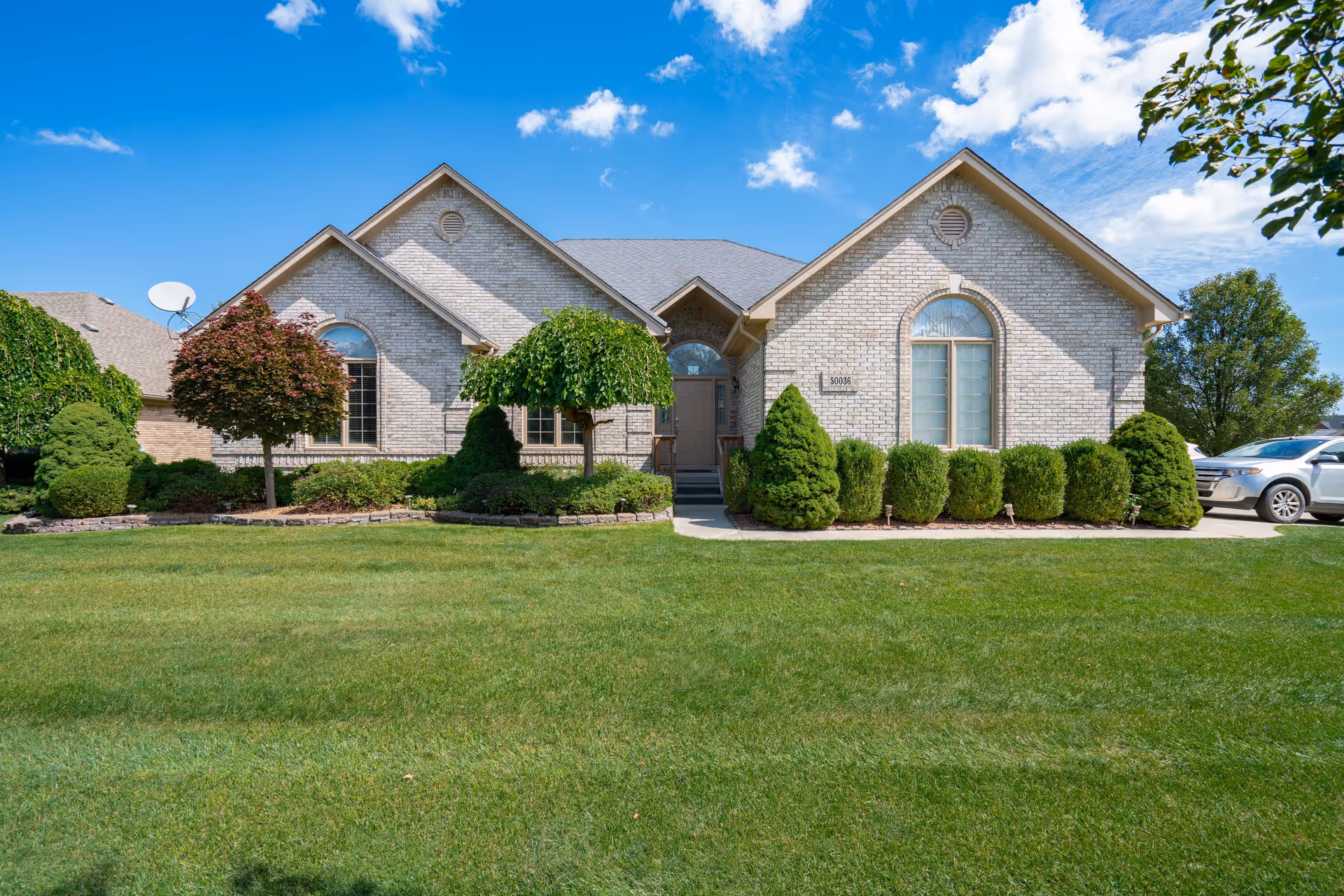 Front exterior view of a single-story brick building with a well-maintained lawn and various shrubs and trees under a blue sky with some clouds.