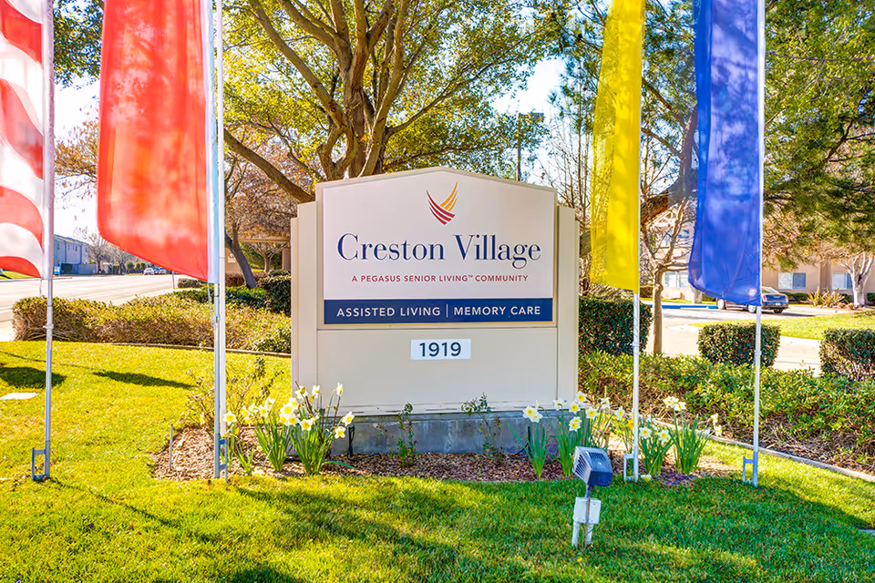 Entrance sign for Creston Village assisted living and memory care surrounded by flags and landscaping.