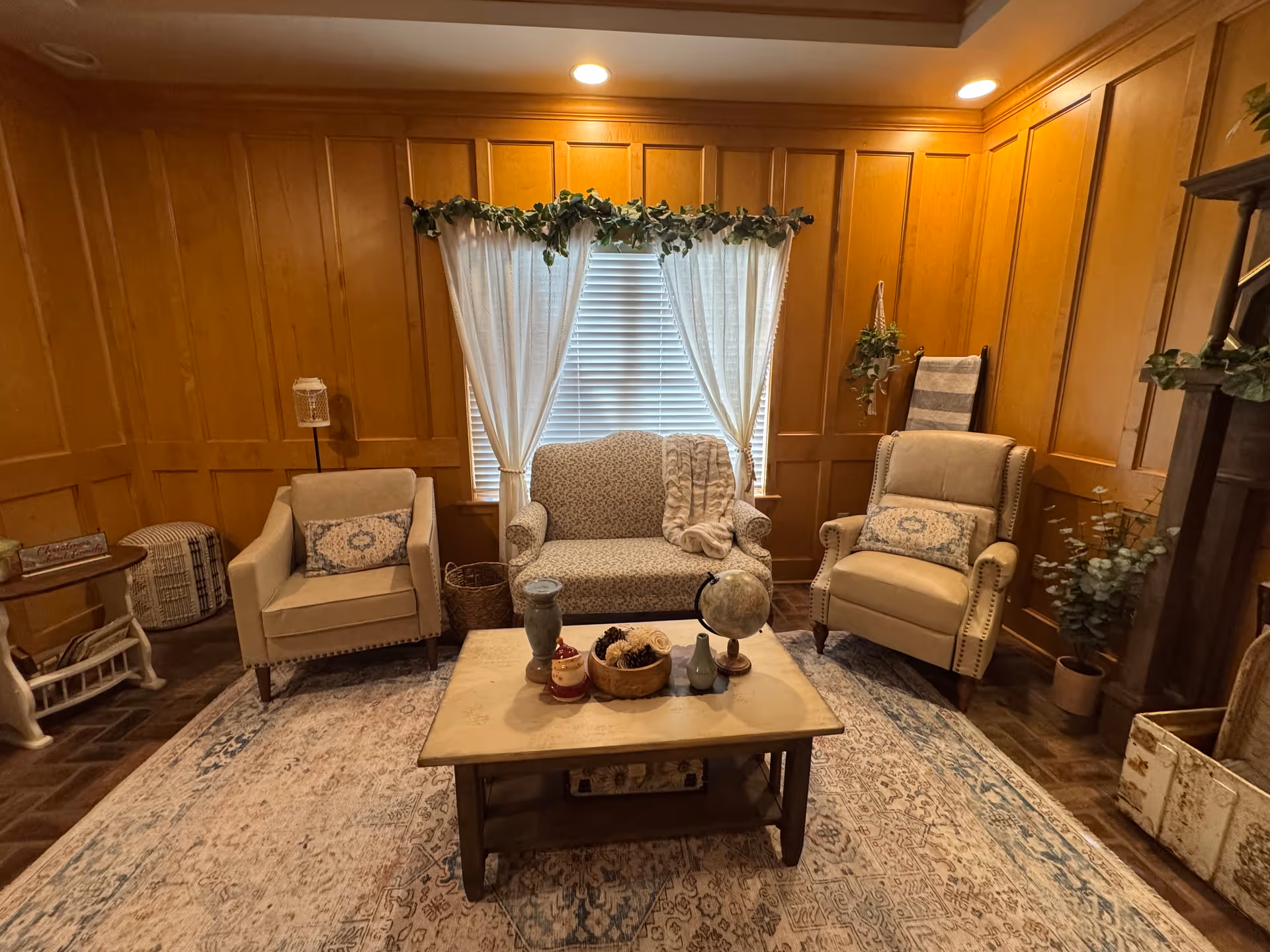 Cozy living room with wood-paneled walls, upholstered chairs, and a central window.