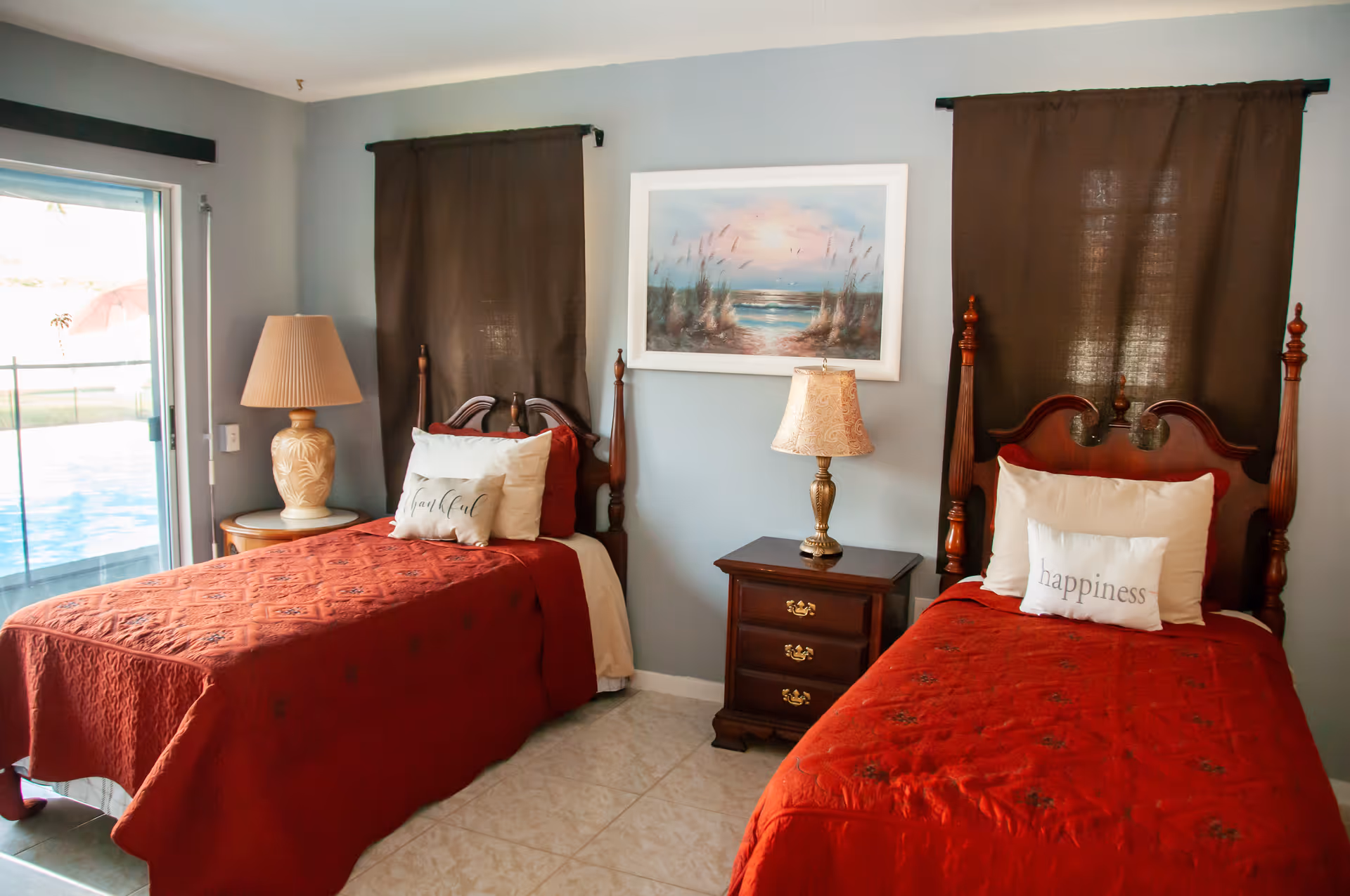 Two twin beds with red quilts and a nightstand in a blue bedroom.
