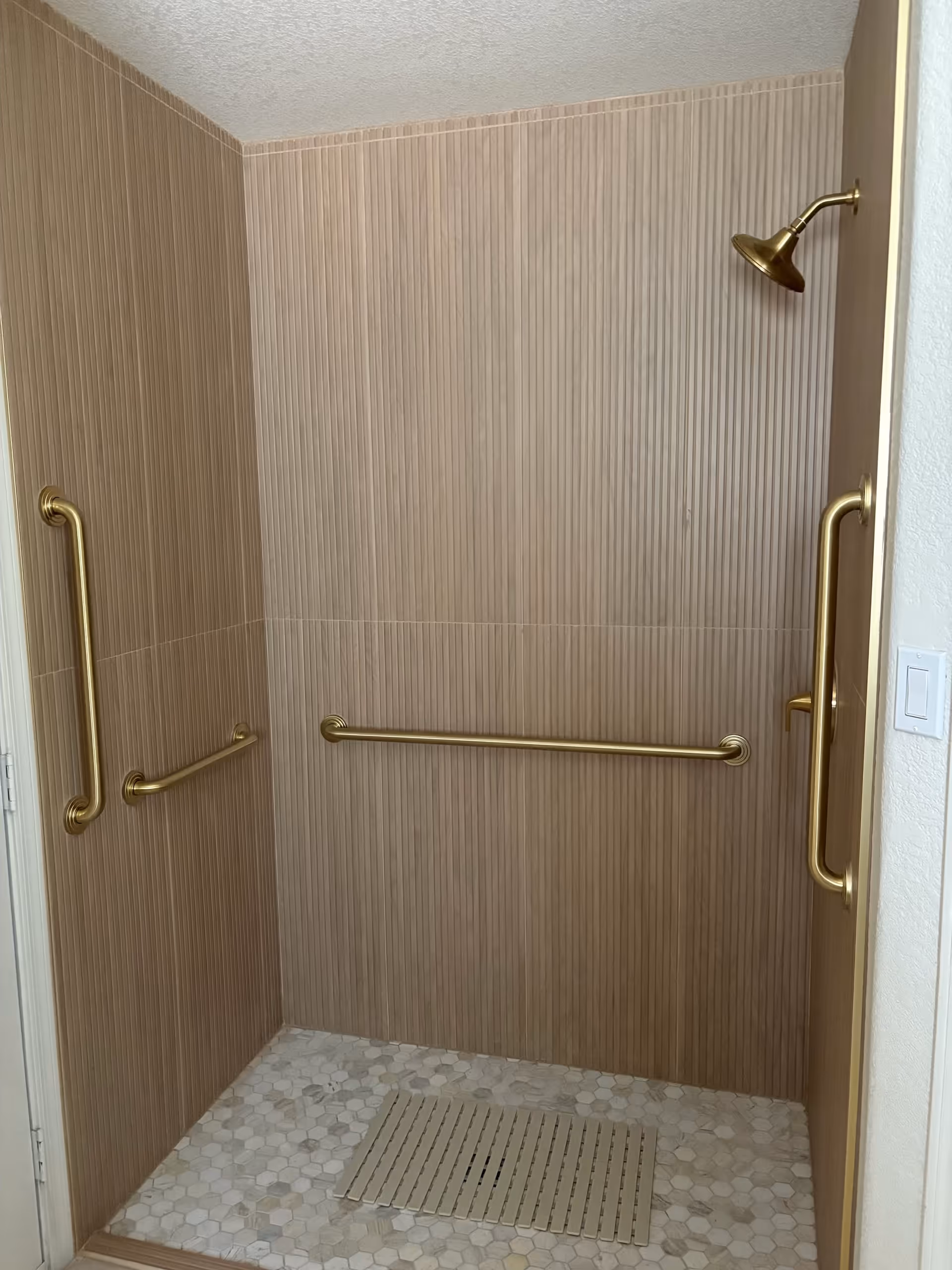 Accessible shower with beige tile walls, brass grab bars, and a wall-mounted shower head.