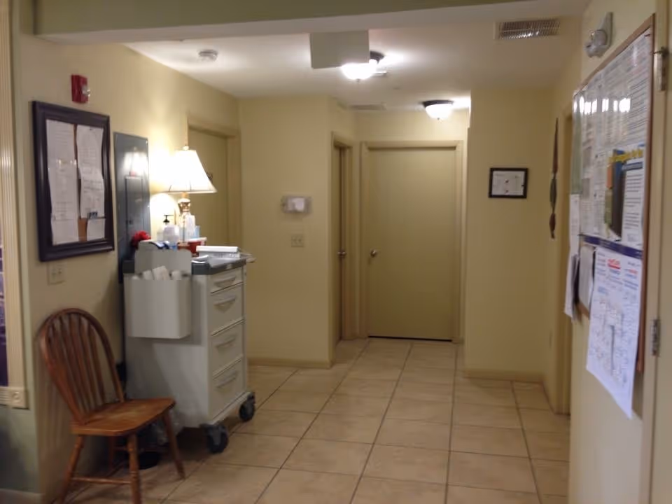 Interior hallway at Heritage ALF of Plant City, with a cart, bulletin board, and a chair.