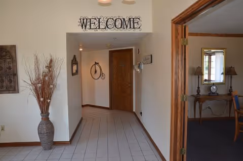 Pine Ridge Health and Rehab lobby hallway with Welcome sign, vase, and doorway to rooms.