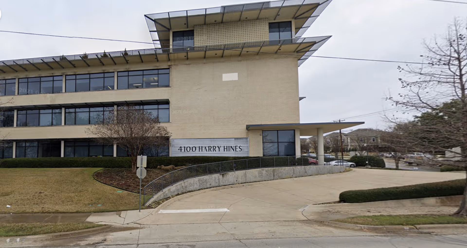 Exterior view of a modern building with a sign reading 4100 HARRY HINES and curved driveway.