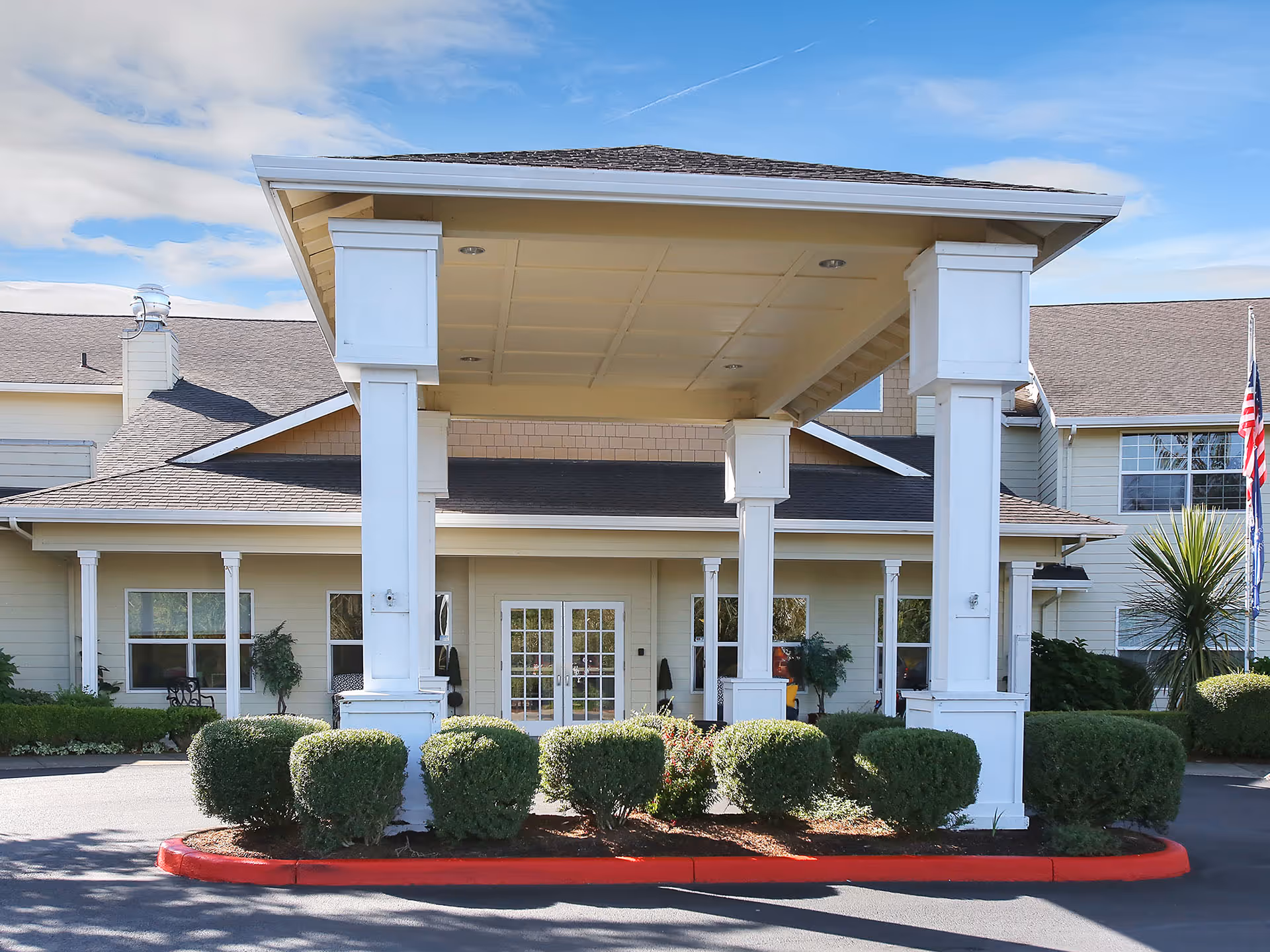Front entrance of Prestige Senior Living Five Rivers with a covered drop-off and shrubs