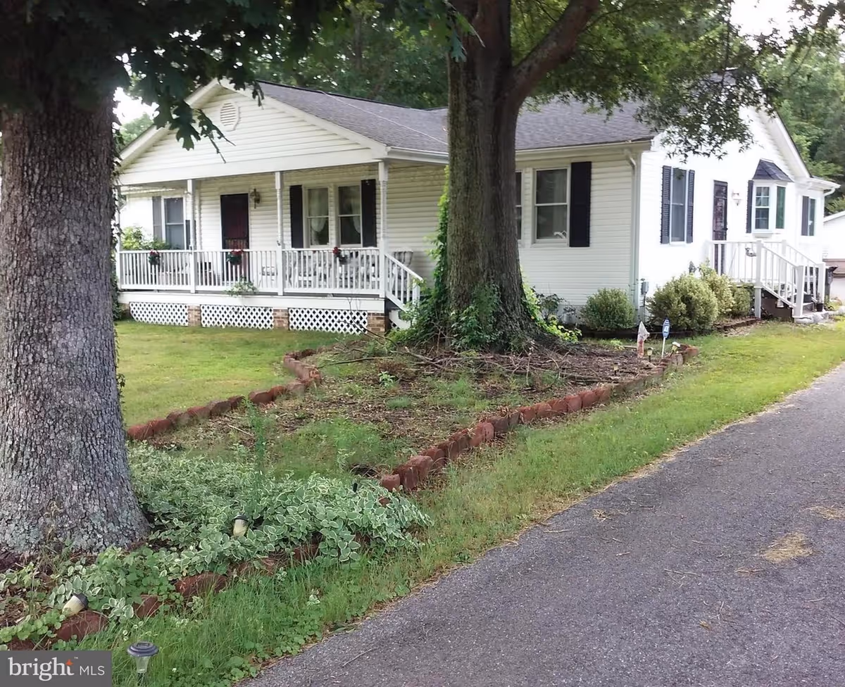 White single-story senior living facility with a wraparound porch and greenery.