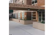 Exterior view of a brick building entrance with Cabrini Apartments sign, planters, and glass doors.