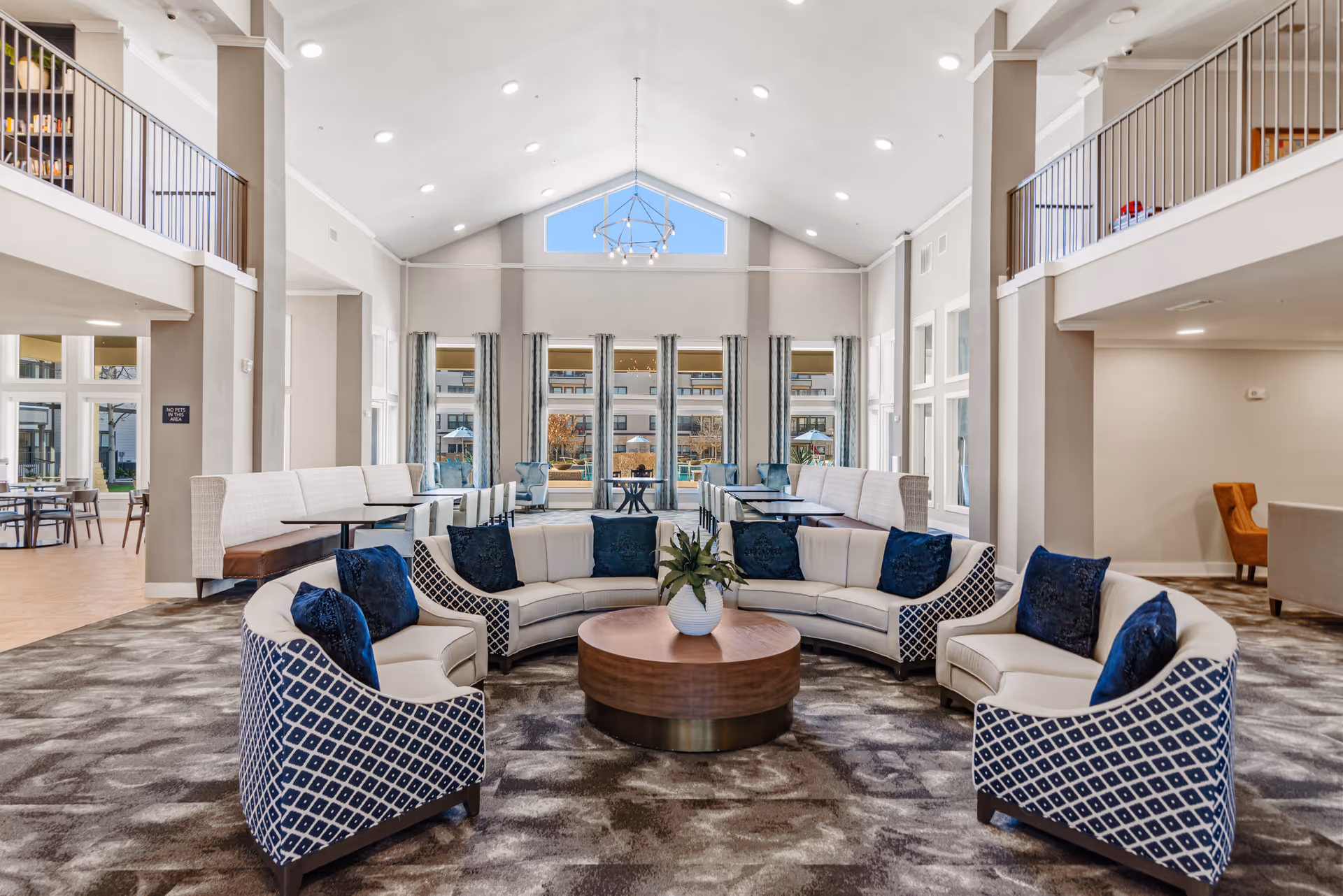 Spacious senior living lobby with curved seating, central table, and expansive windows.