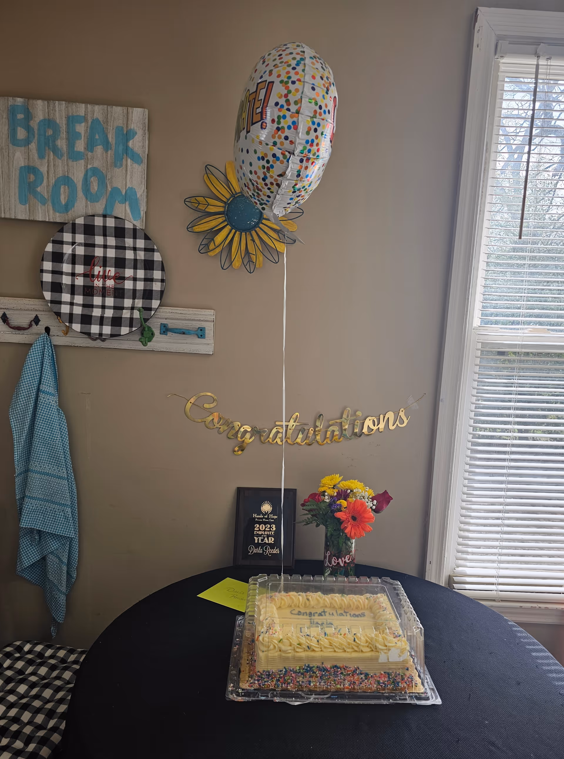 Celebration setup inside a bright room with cake, balloons, flowers, and a Break Room sign.
