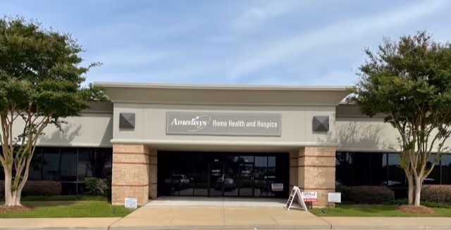 Front exterior view of Amedisys Home Health and Hospice building with glass doors and trees.
