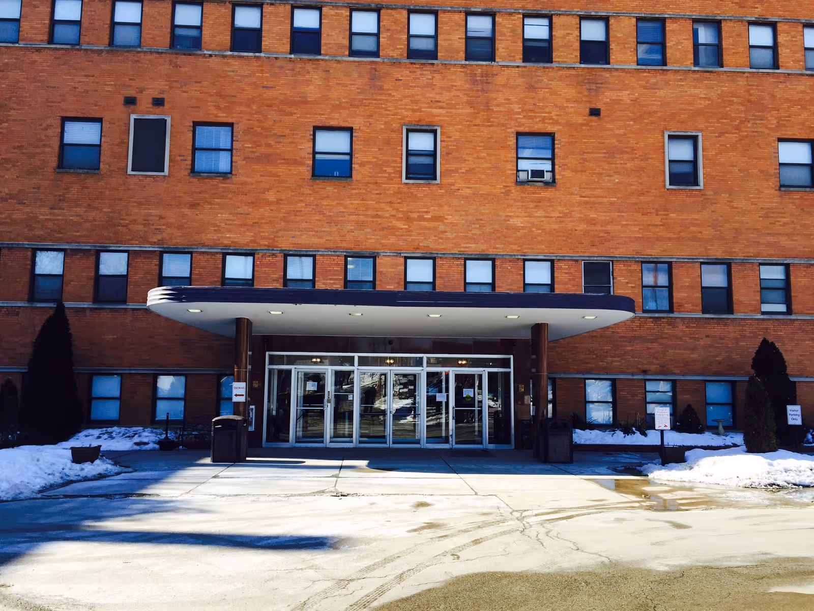 Entrance to Village at Pennwood senior living facility with glass doors beneath a curved canopy.