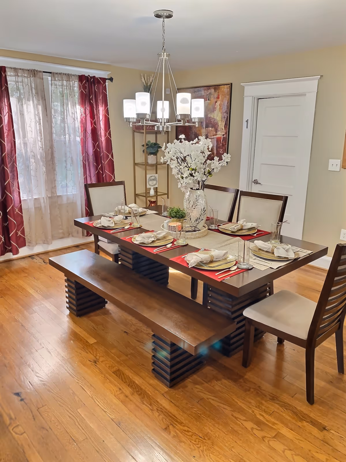 A dining room with a large table set for six, chandelier, and red curtains.