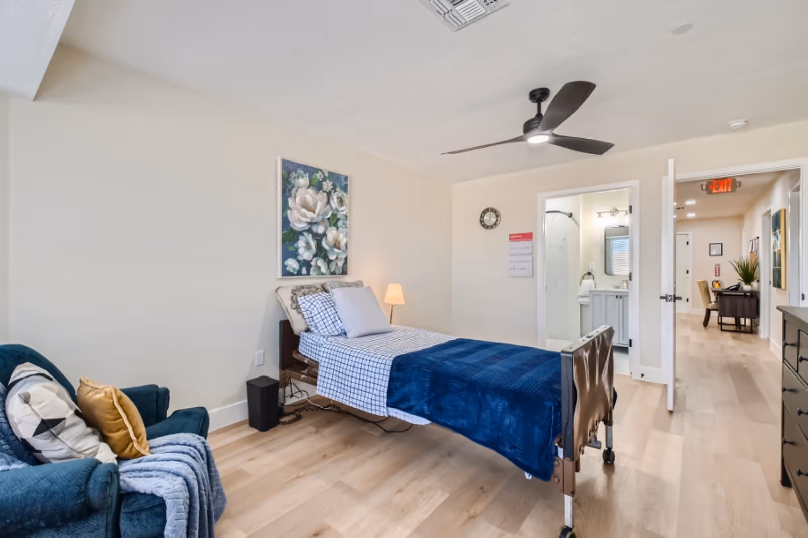 Bright senior living bedroom with a hospital-style bed, blue blanket, and seating area.