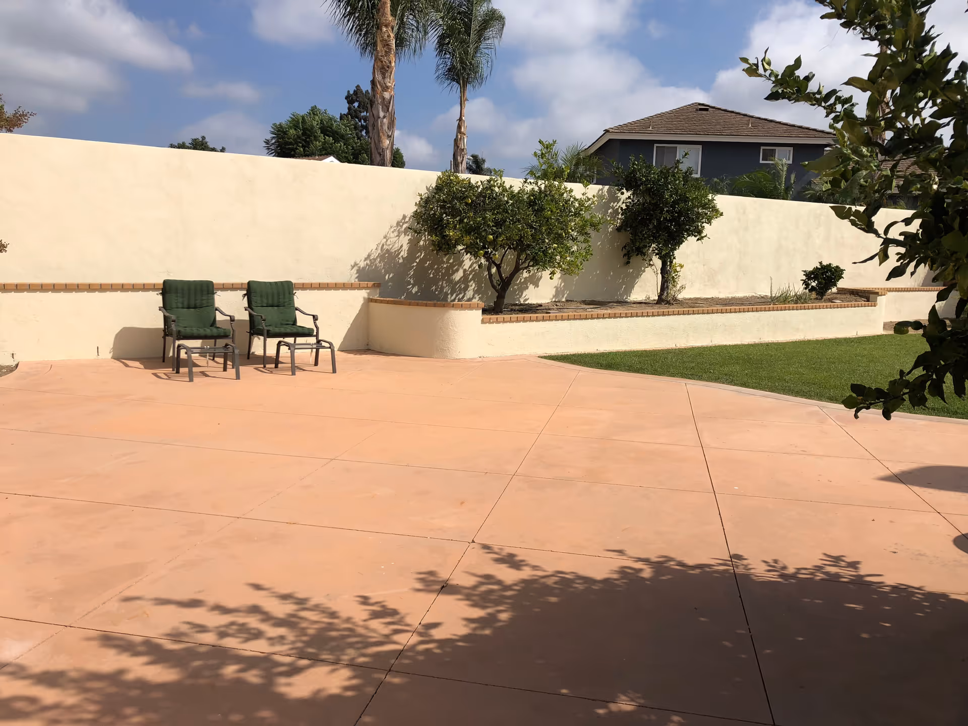 Outdoor patio with two green chairs beside a beige wall and small garden planters.