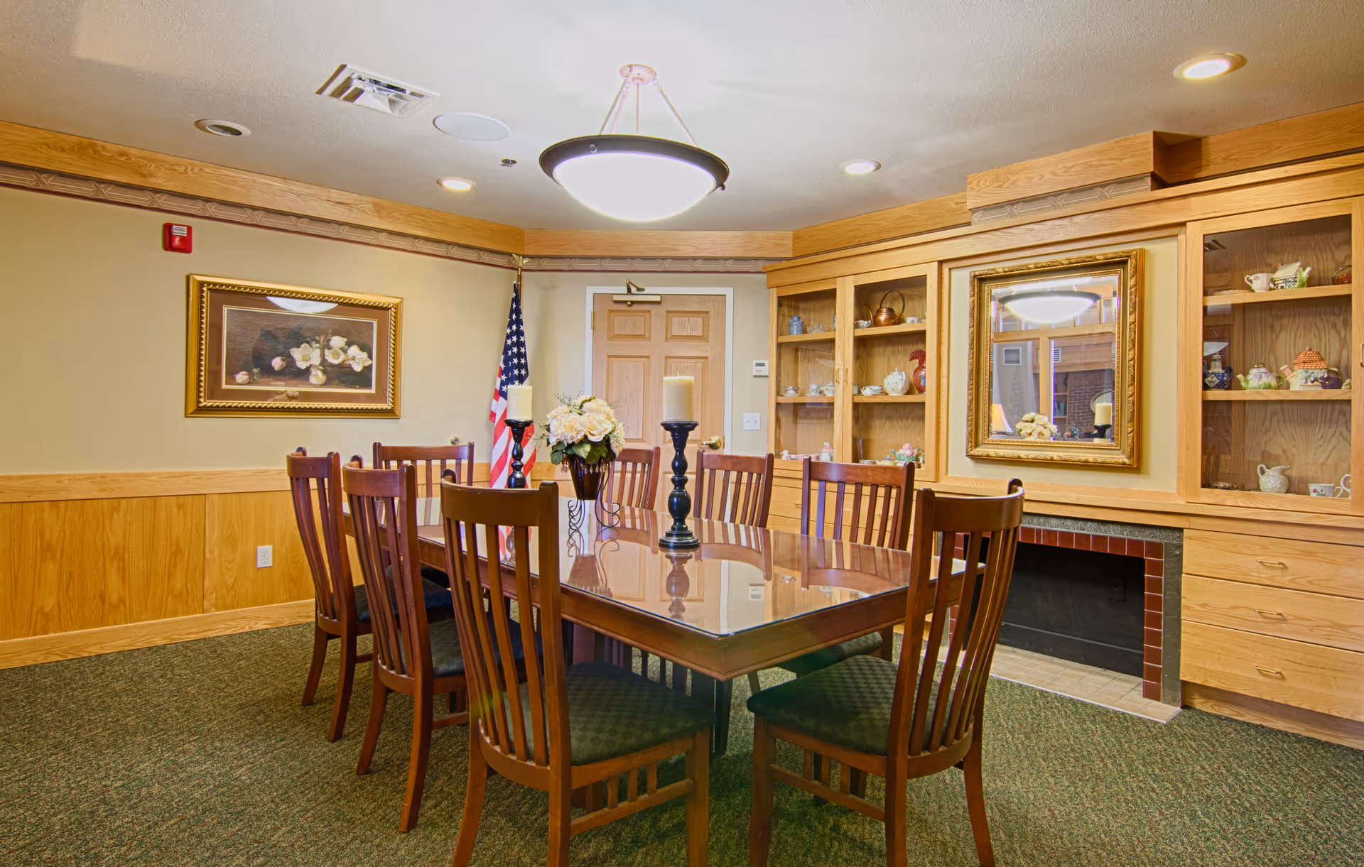 A wood dining room with a long table, chairs, cabinets, and floral centerpiece.
